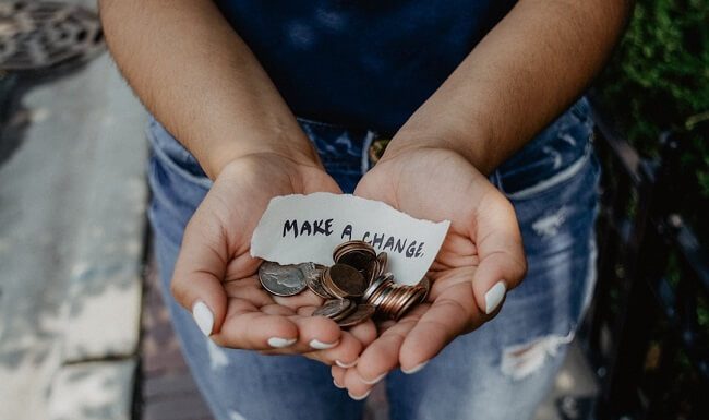 A person holds change and a strip of paper reading "Make a change"